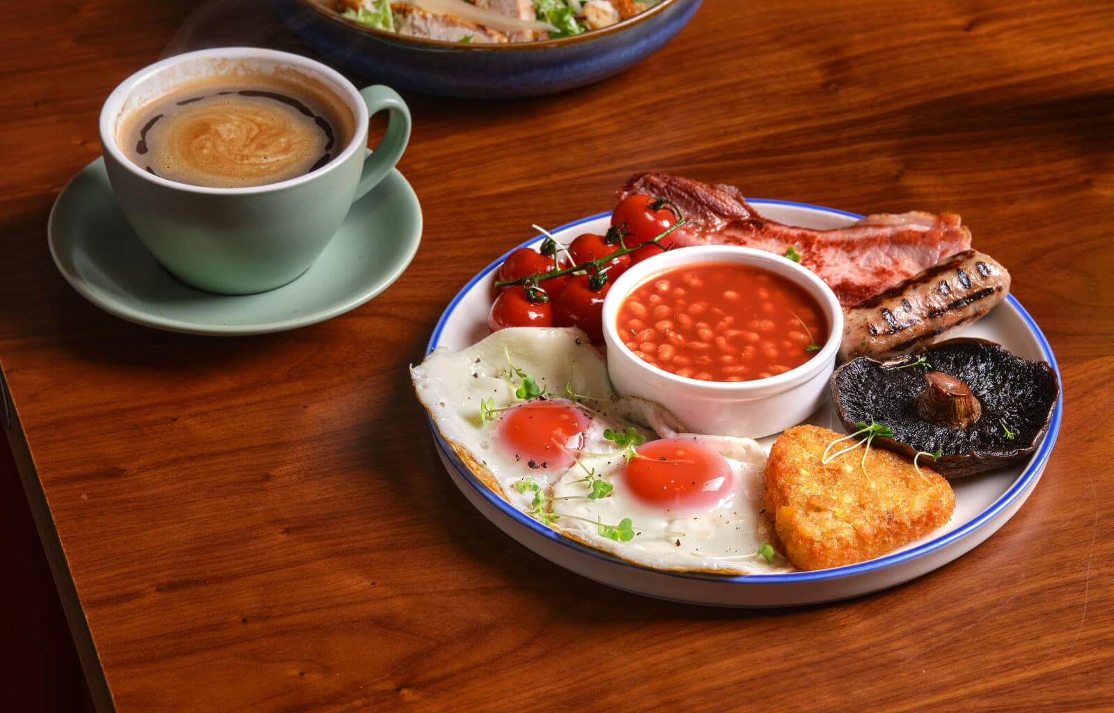 A full English breakfast and a coffee on a walnut table