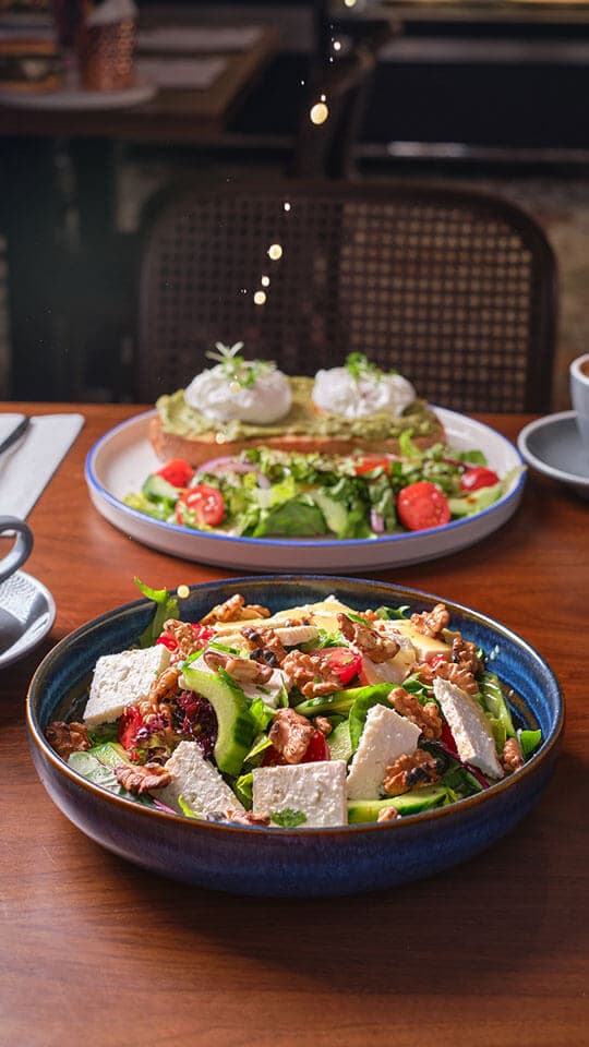 A feta salad and eggs benedict on a table by the window